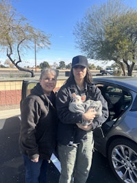 two people standing in front of a car holding a baby