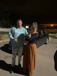 a man and woman standing in front of a car at night