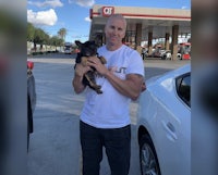 a man holding a dog in front of a gas station
