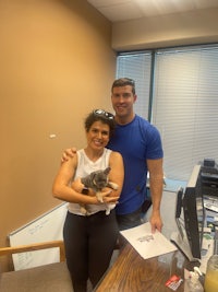 a man and woman standing in front of a desk with a cat
